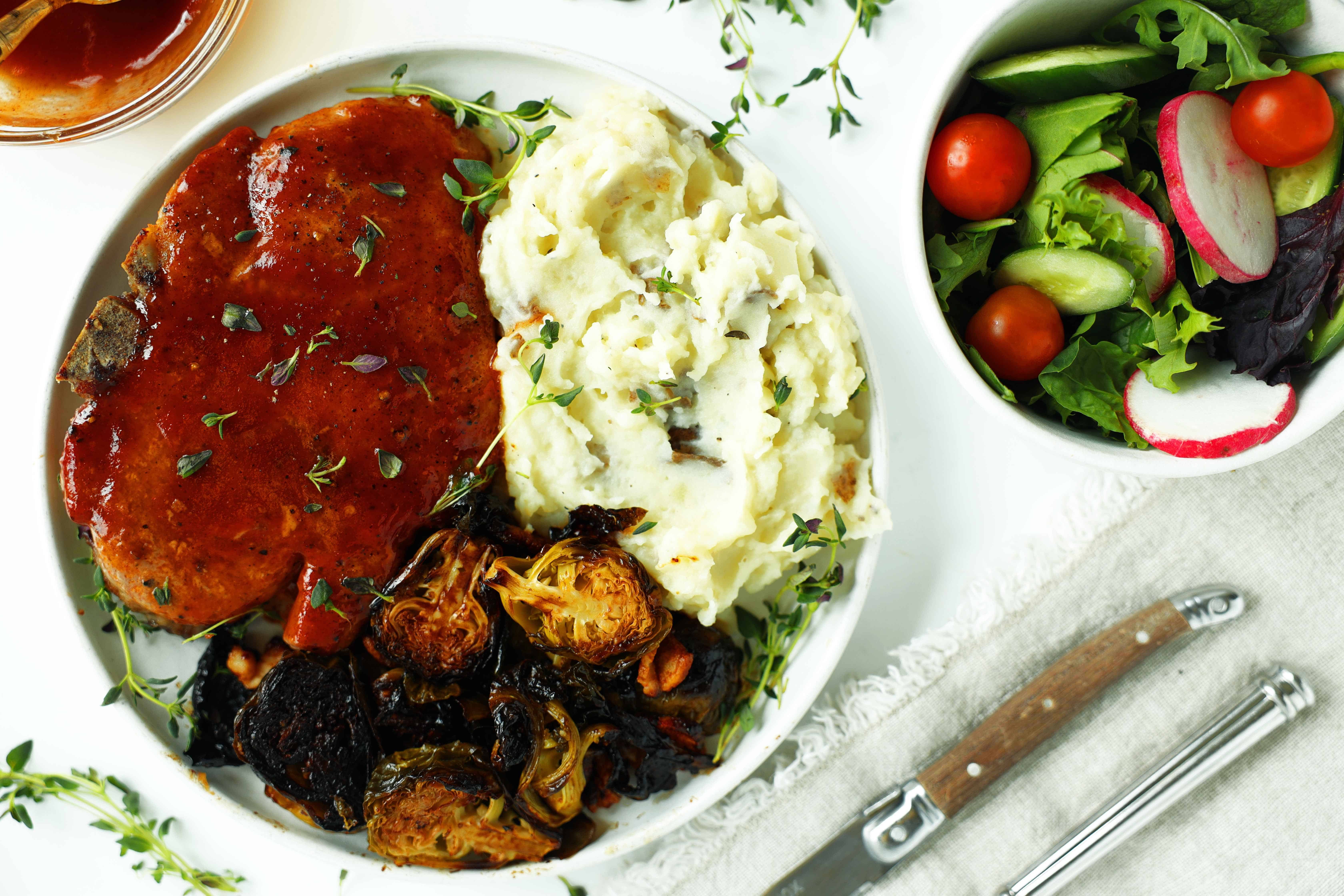 Dinner plate with a BBQ pork chop, mashed potatoes, and caramelized Brussels sprouts.