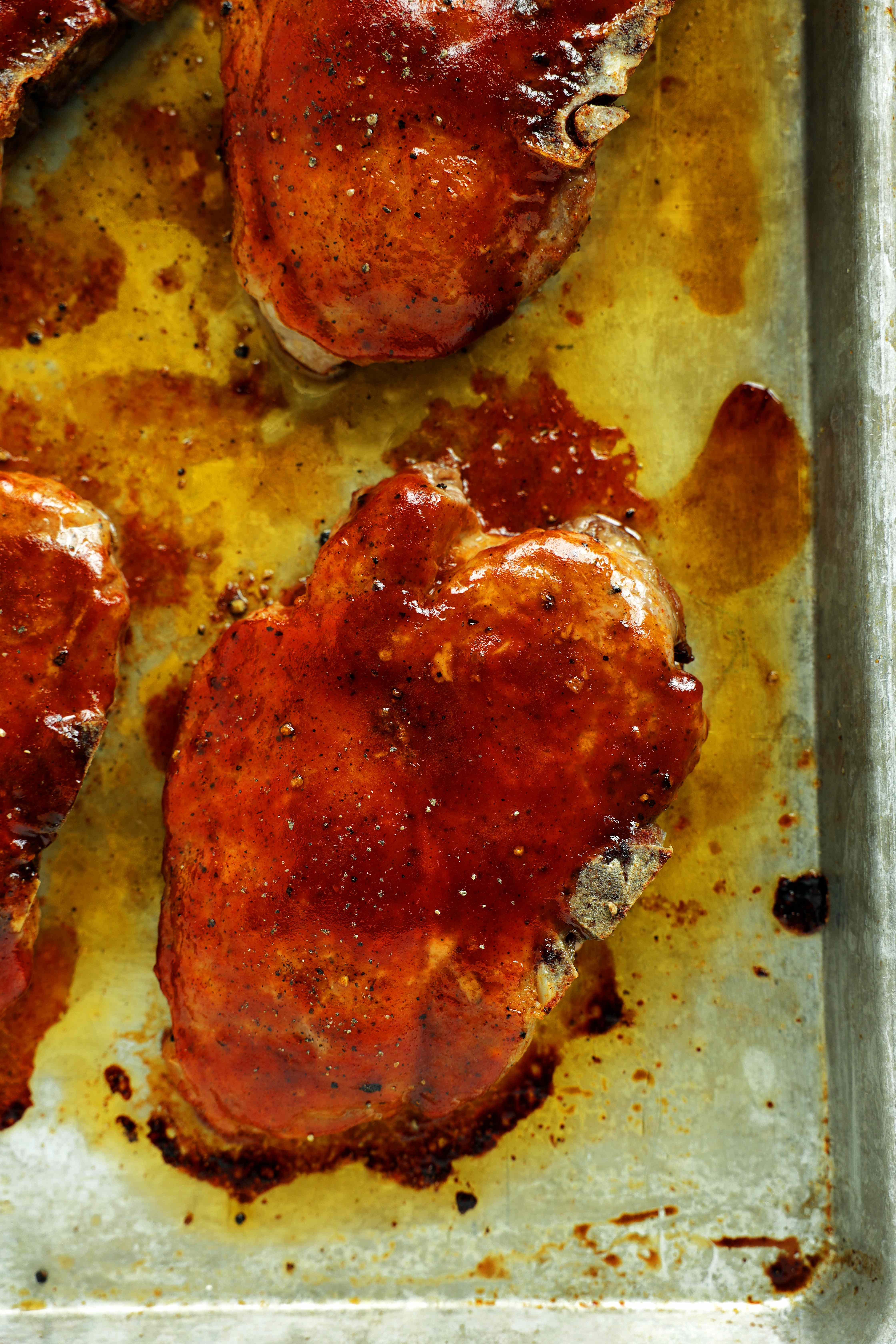 Baked BBQ pork chops coated in barbecue sauce on a rimmed baking sheet.