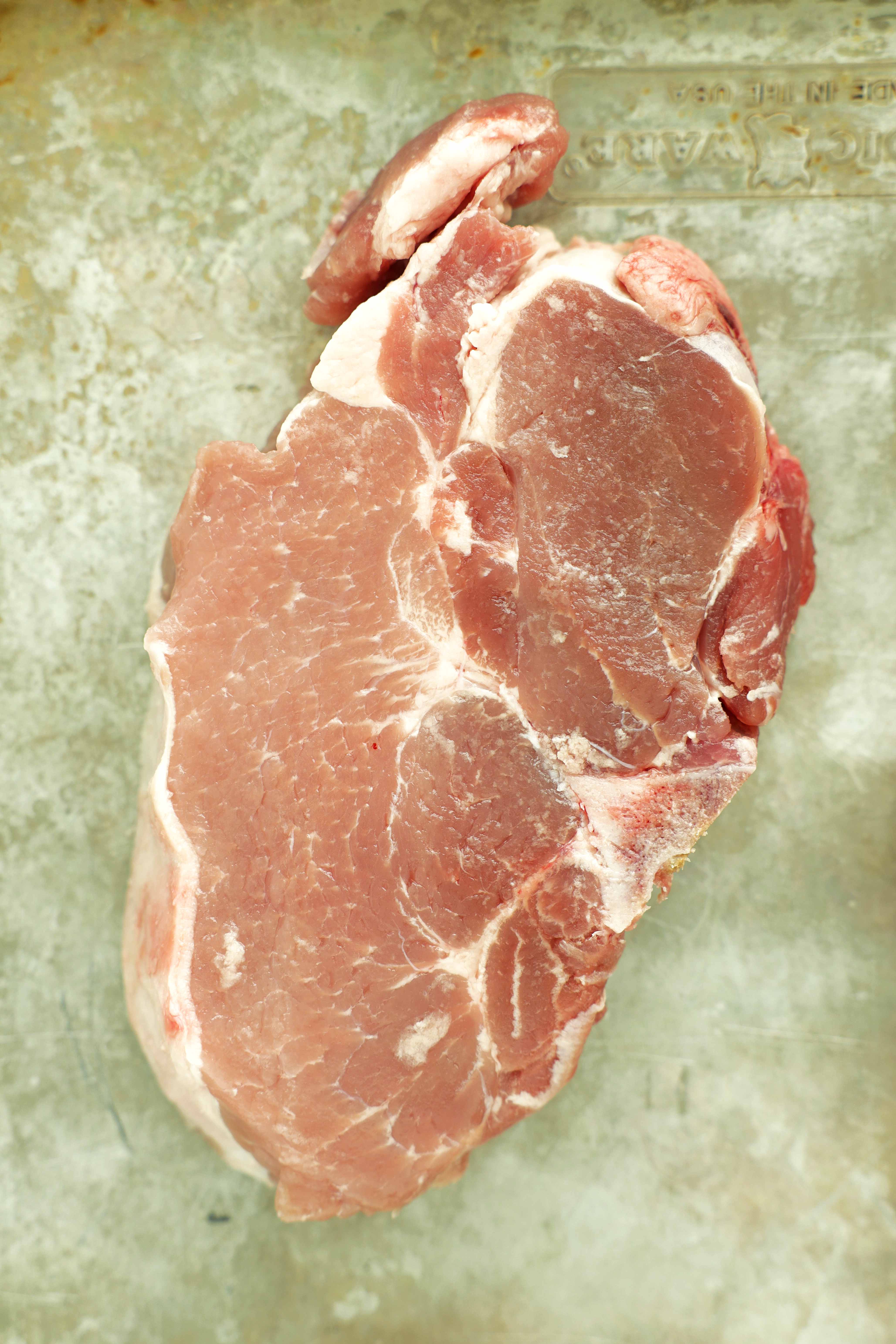 Single raw bone-in pork chop on a baking sheet.