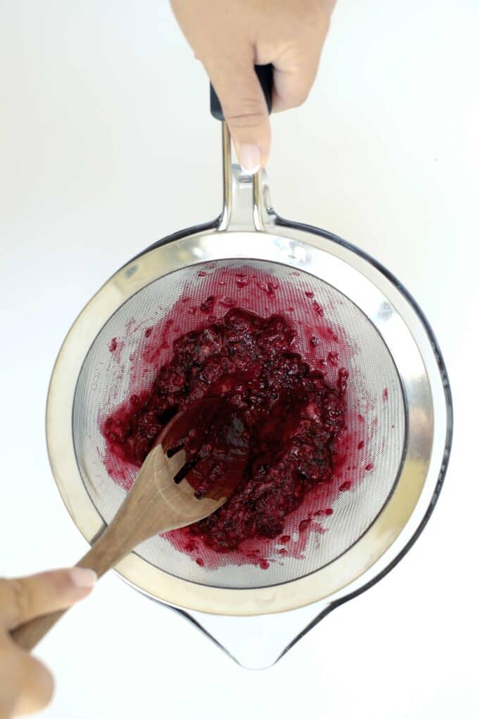 Mashing blackberries in a fine-mesh strainer for making blackberry simple syrup
