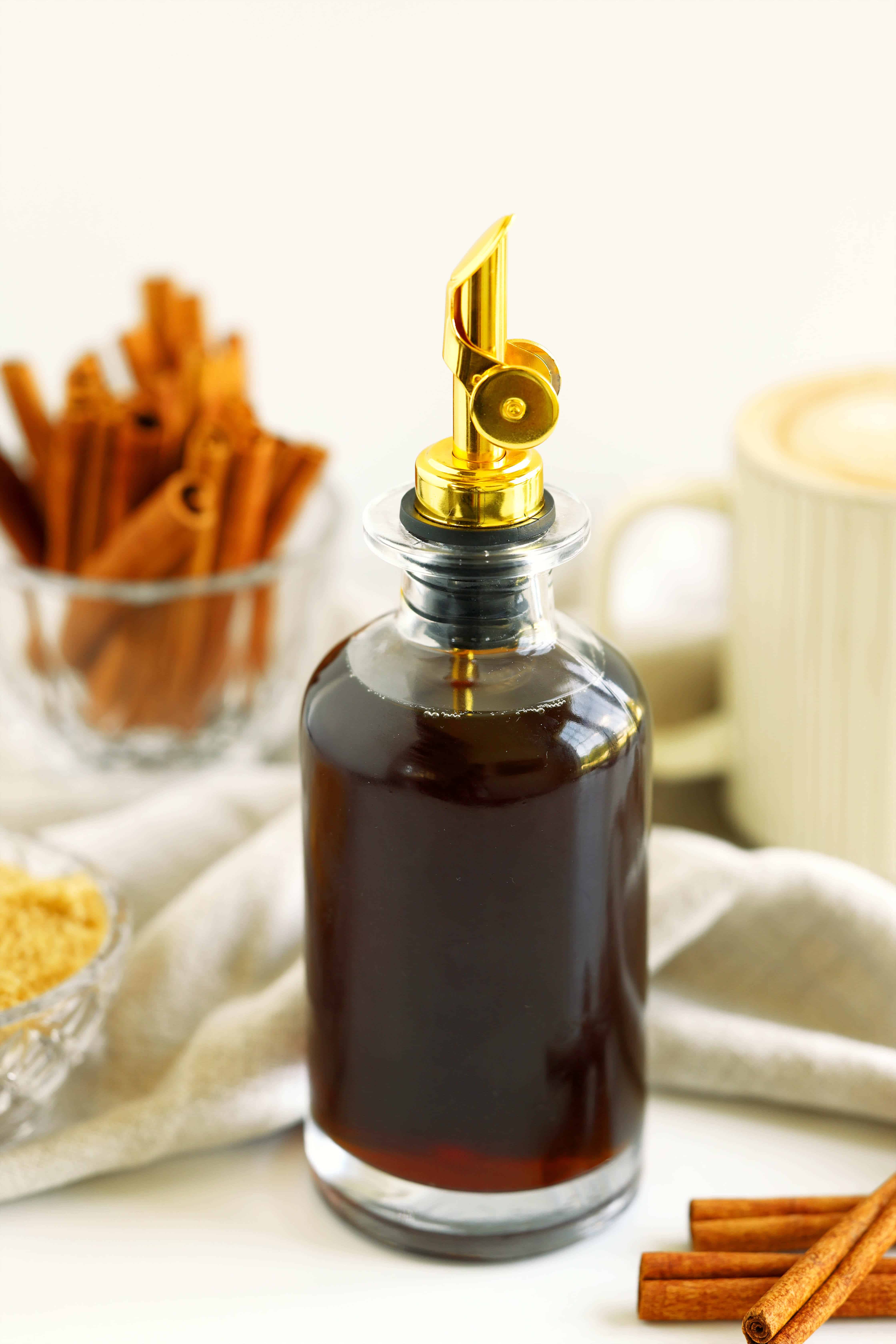 Homemade cinnamon syrup in a glass bottle with brown sugar, cinnamon sticks, and coffee in the background.