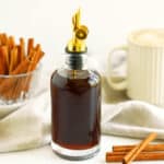 Homemade cinnamon syrup in a glass bottle with brown sugar, cinnamon sticks, and coffee in the background.