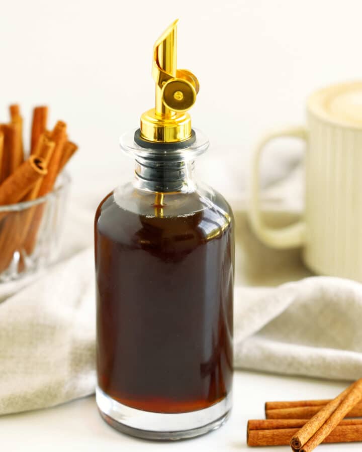 Homemade cinnamon syrup in a glass bottle with brown sugar, cinnamon sticks, and coffee in the background.
