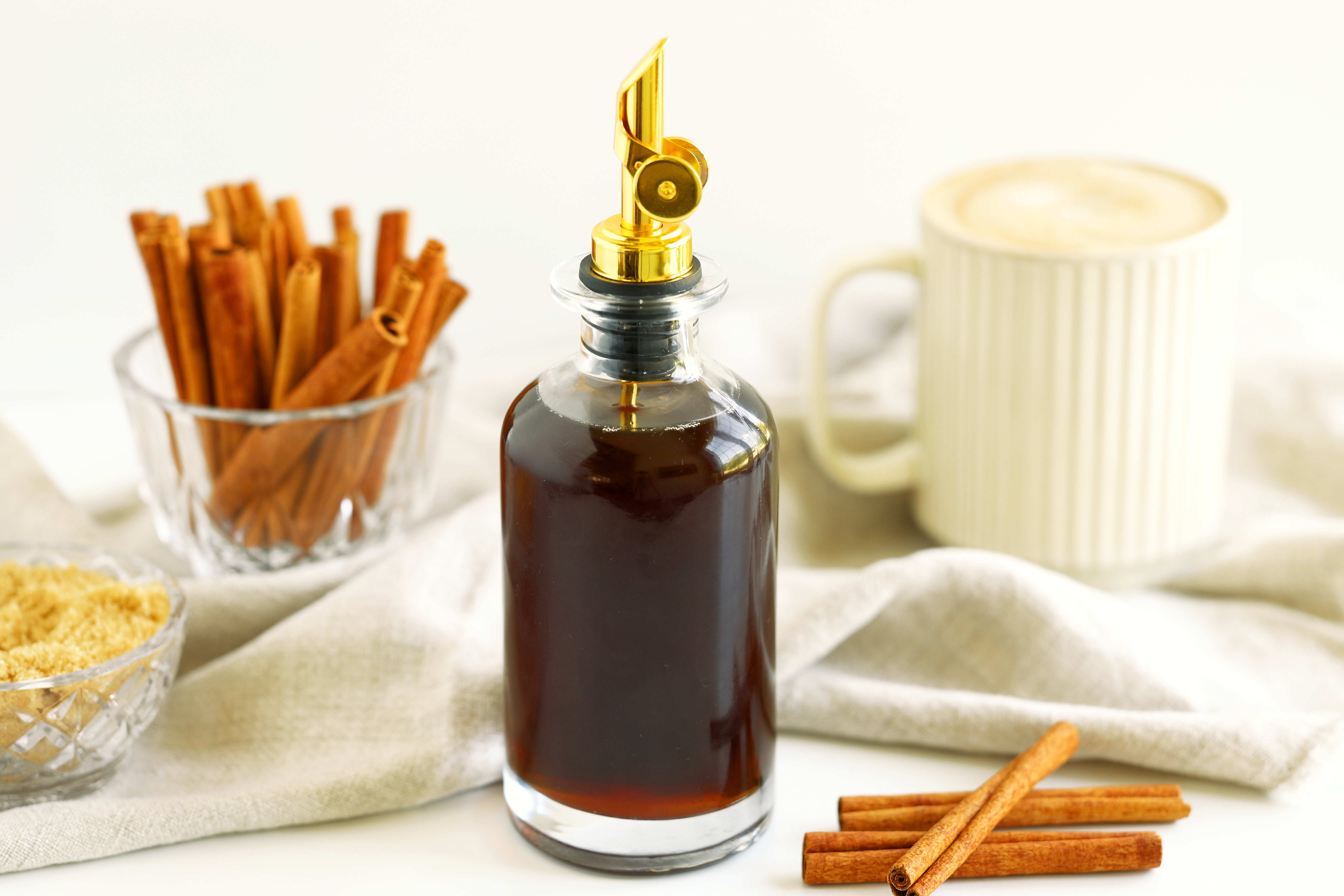 Cinnamon syrup beside a whipped cream topped coffee cocktail with cinnamon sticks in the background.