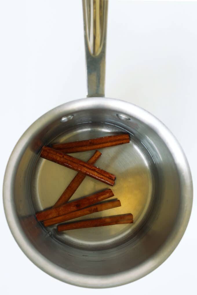 Cinnamon sticks simmering in water in a small saucepan to make homemade cinnamon syrup.