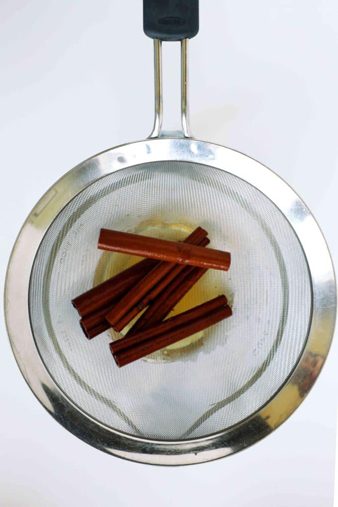 Cinnamon sticks being strained from infused water while making cinnamon syrup.