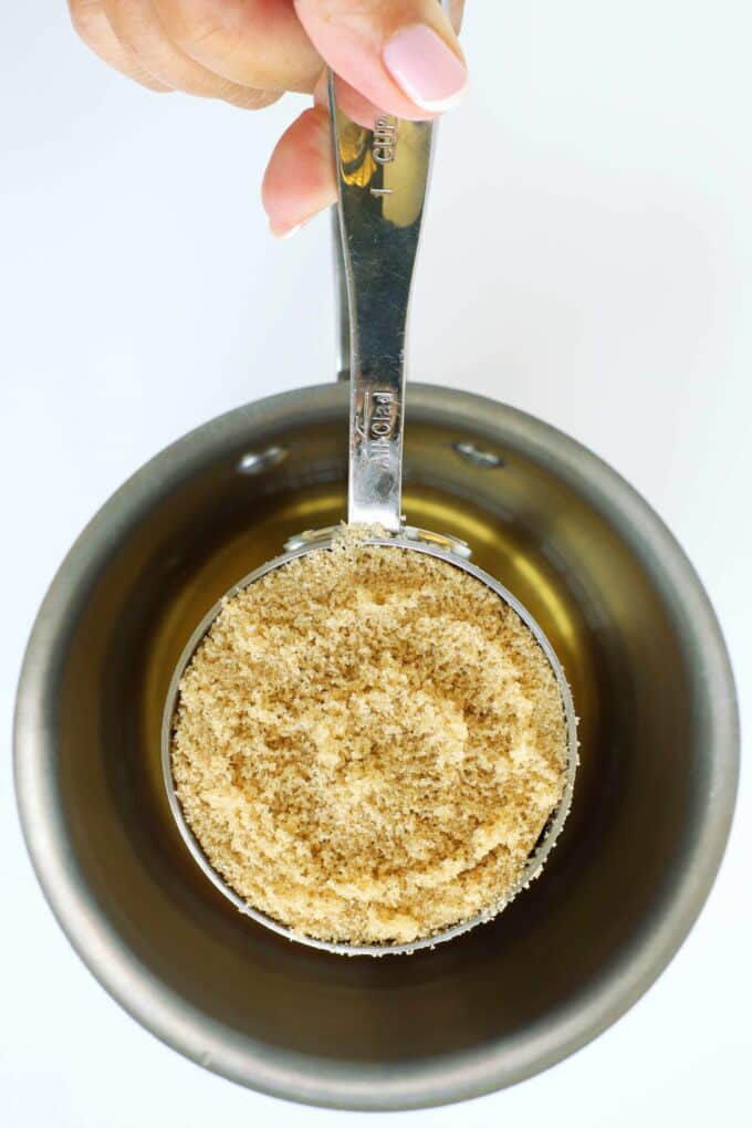 Light brown sugar being added to cinnamon infused water in a saucepan.