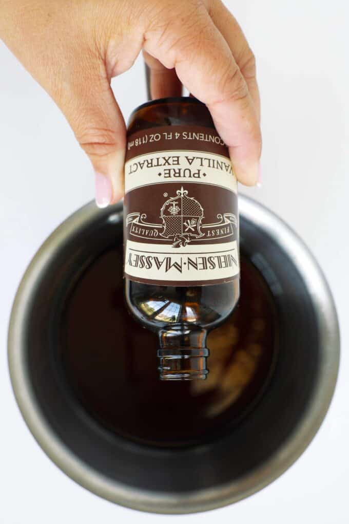 Vanilla extract being added to homemade cinnamon syrup in a saucepan.