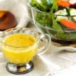 Homemade Dijon dressing in a glass gravy boat beside a bowl of fresh green salad