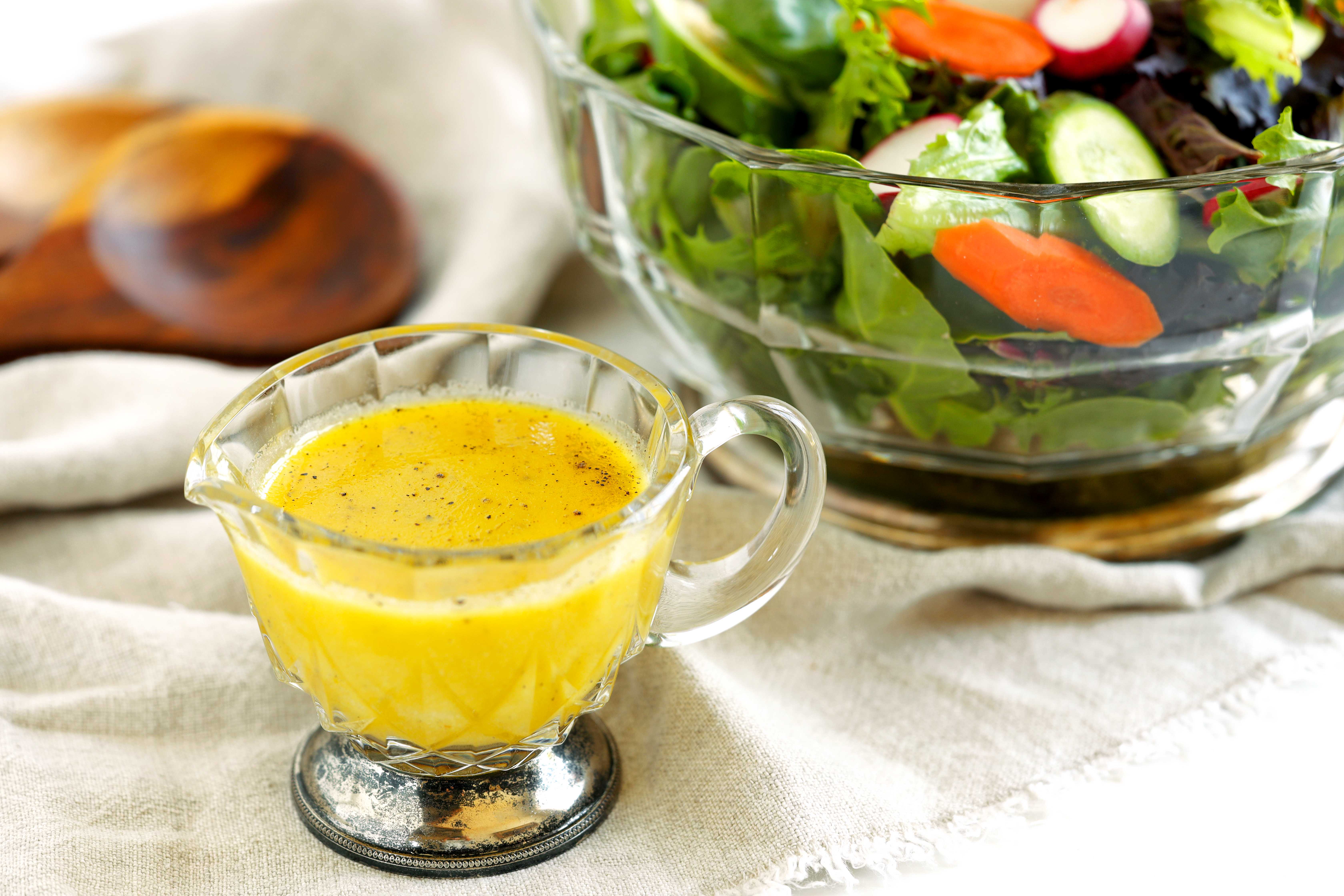 Homemade Dijon dressing in a glass gravy boat beside a bowl of fresh green salad