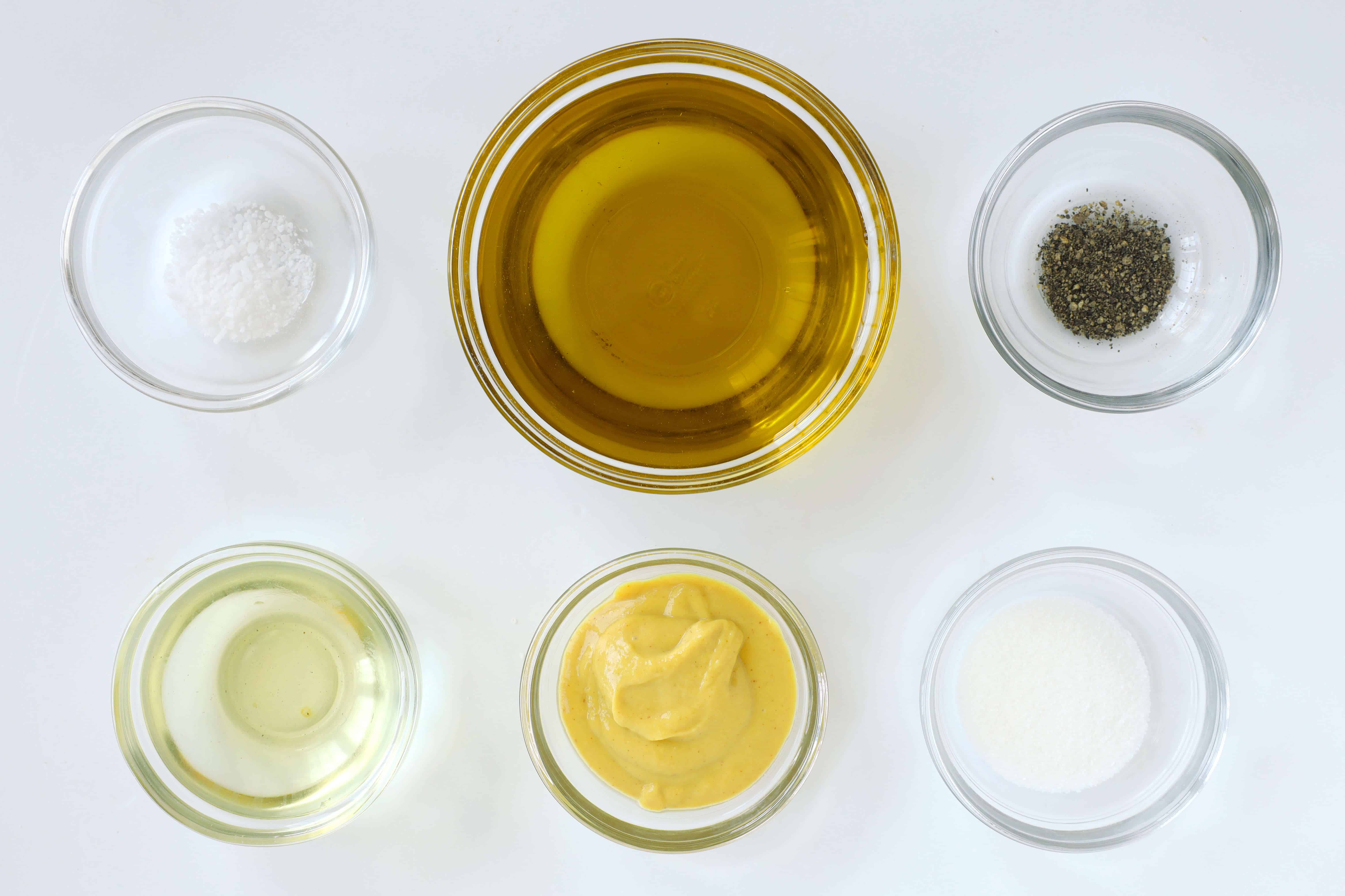 Ingredients for homemade Dijon dressing including olive oil, tarragon vinegar, Dijon mustard, sugar, salt, and pepper