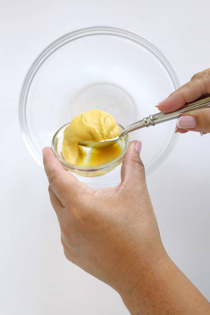 Adding Dijon mustard to a mixing bowl to make homemade Dijon dressing