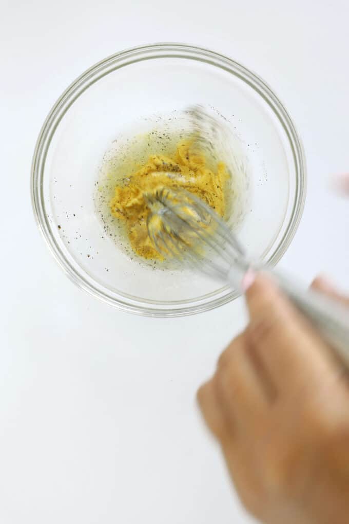 Whisking Dijon mustard, vinegar, garlic, salt, pepper, and sugar for homemade dressing