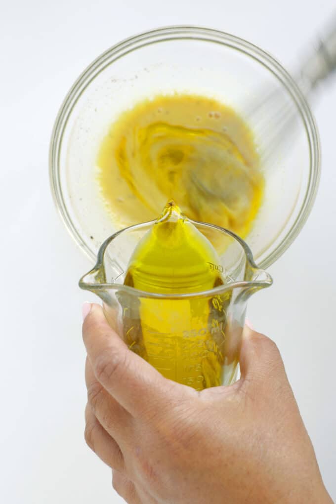 Slowly pouring olive oil into Dijon dressing while whisking to emulsify