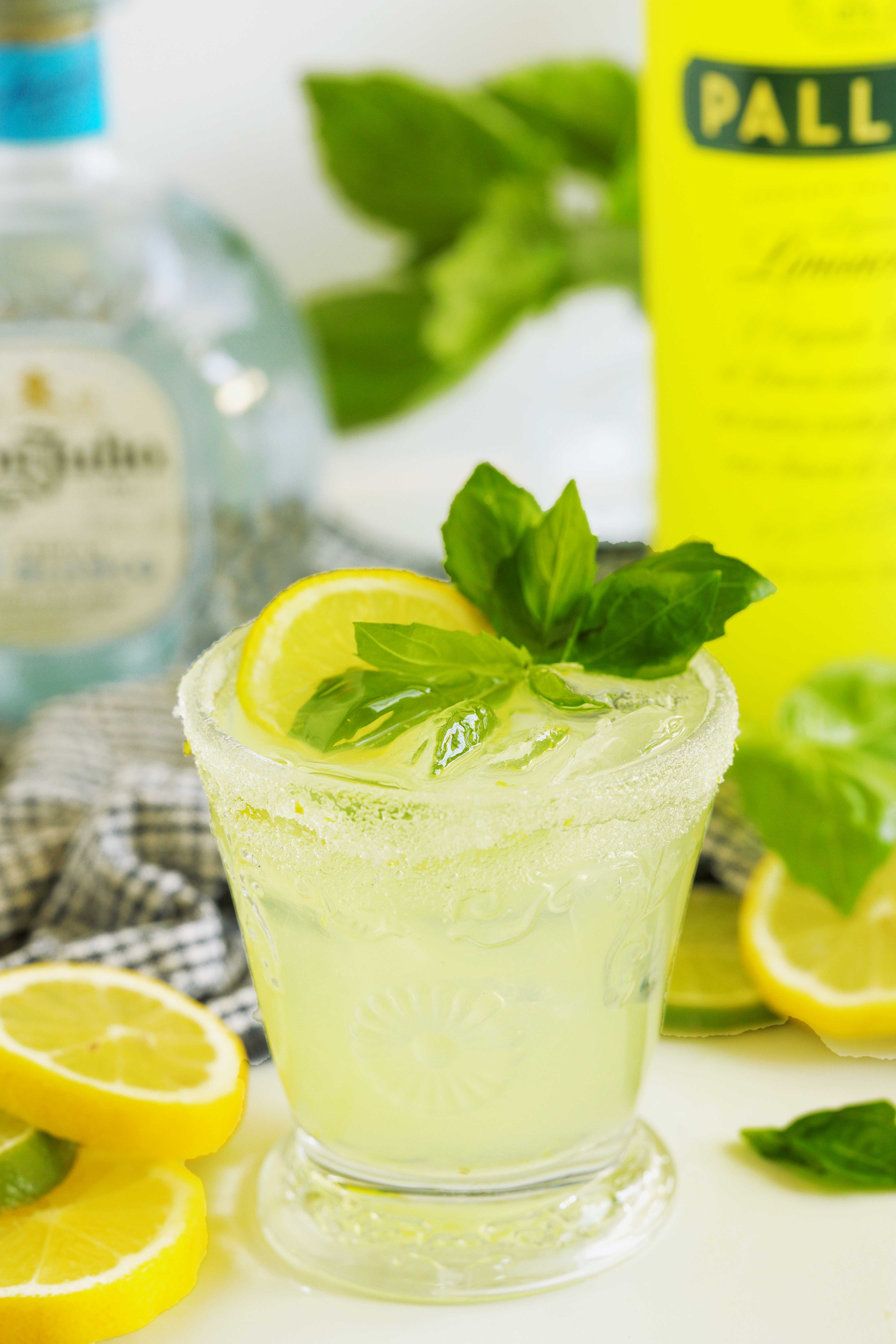 Limoncello margarita with fresh basil and lemon served beside a bottle of limoncello