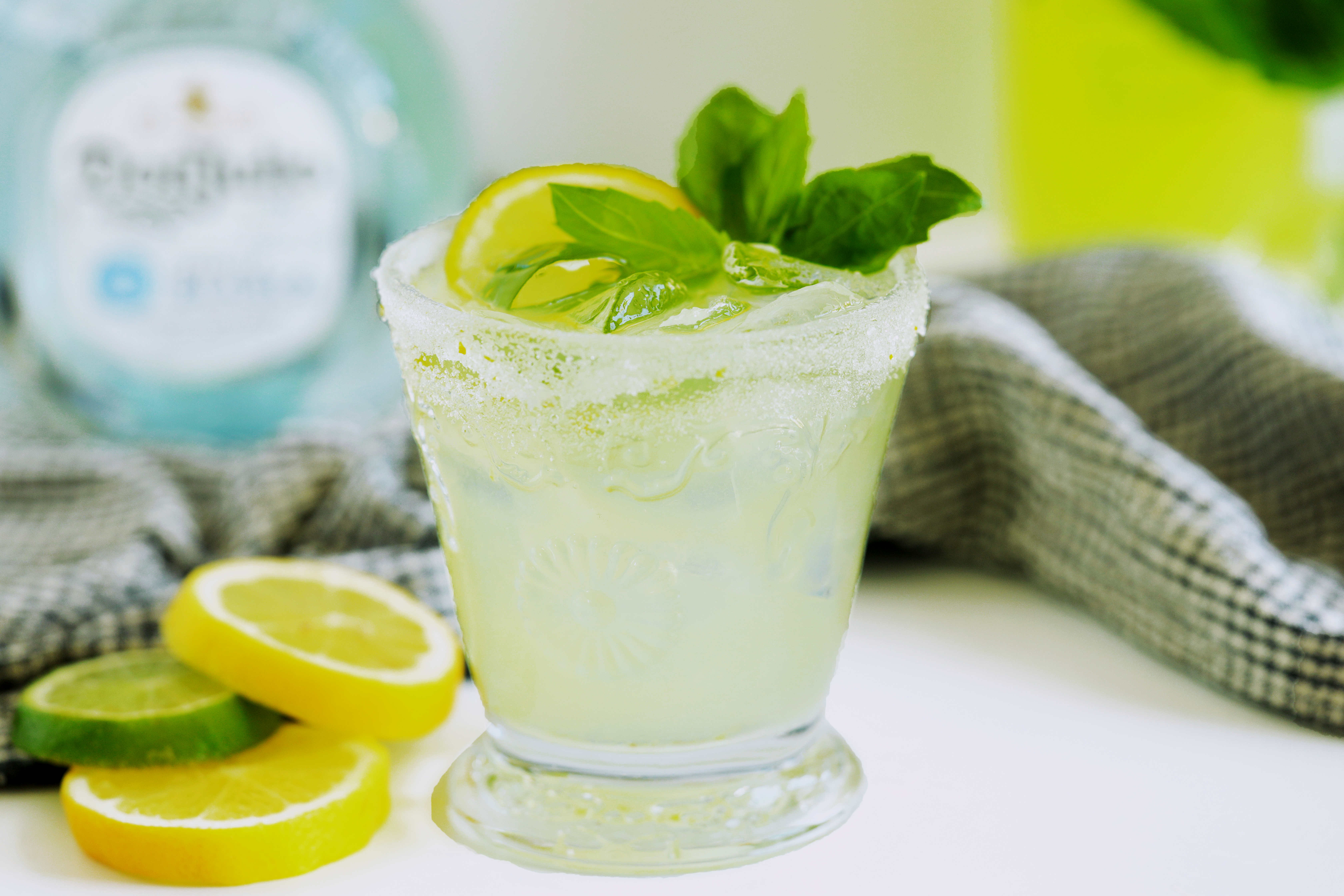 Limoncello margarita garnished with fresh lemon and basil beside sliced citrus