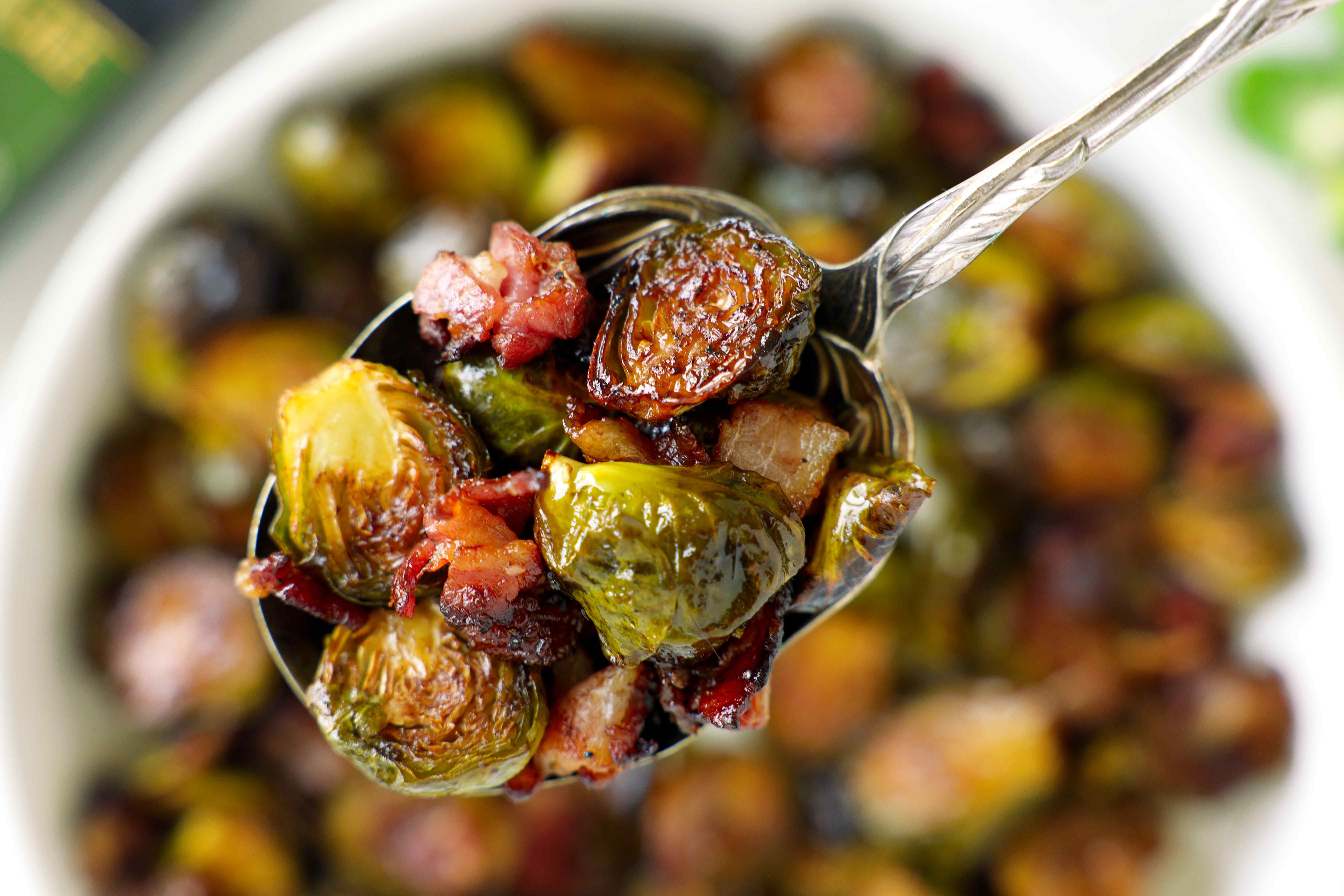 Spoonful of crispy roasted Brussels sprouts with bacon over a white serving dish