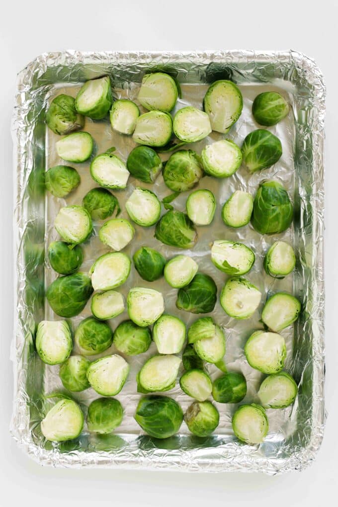 Halved and quartered Brussels sprouts arranged on a foil-lined baking sheet
