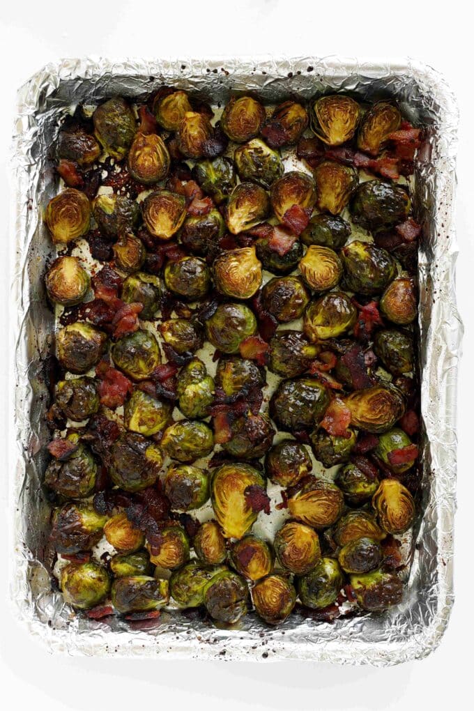 Fully roasted Brussels sprouts with crispy bacon and browned edges on a foil-lined sheet pan