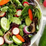 Spring mix salad with cucumbers, radishes, carrots, and Dijon vinaigrette in a white serving bowl
