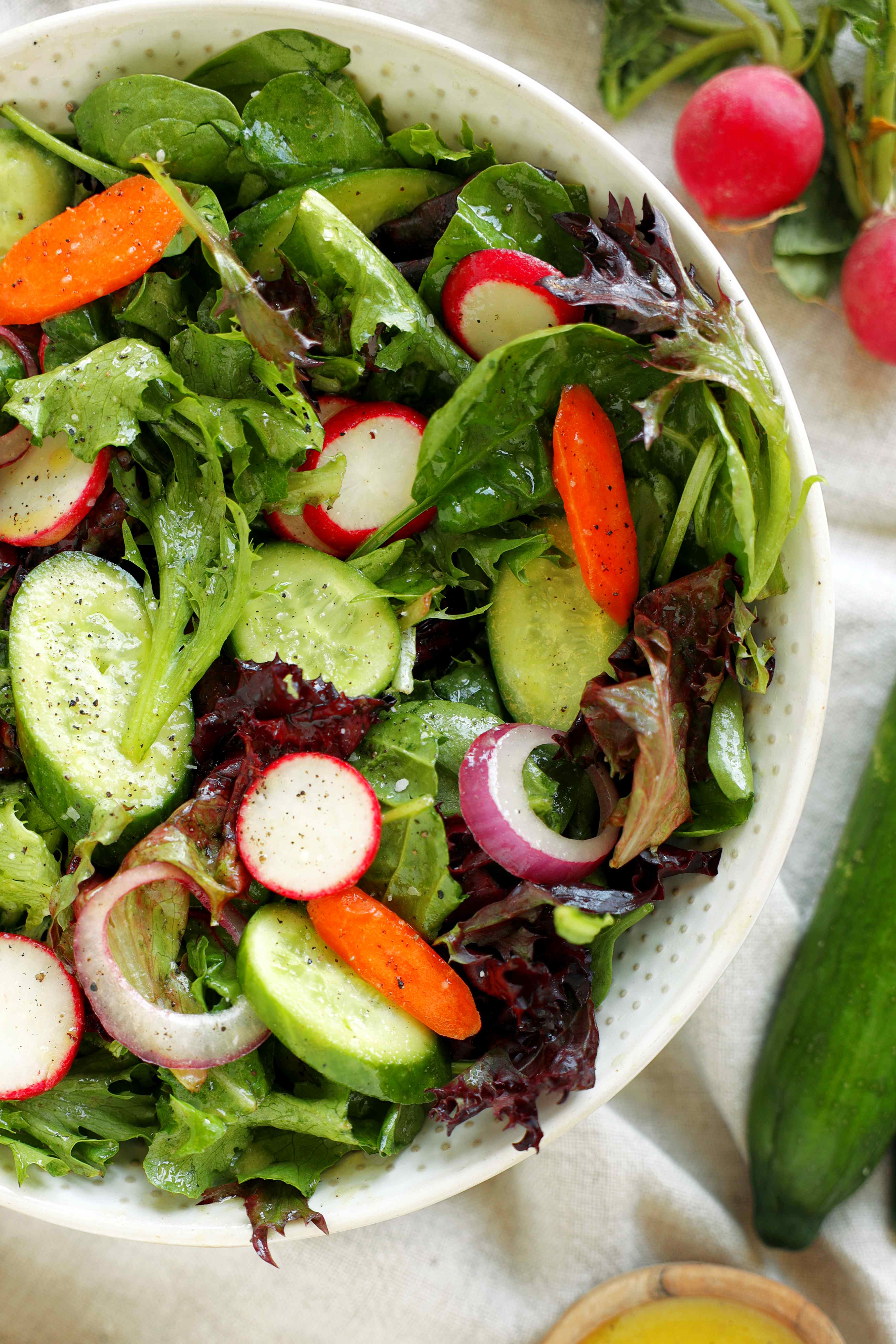 Spring mix salad with cucumbers, radishes, carrots, and Dijon vinaigrette in a white serving bowl