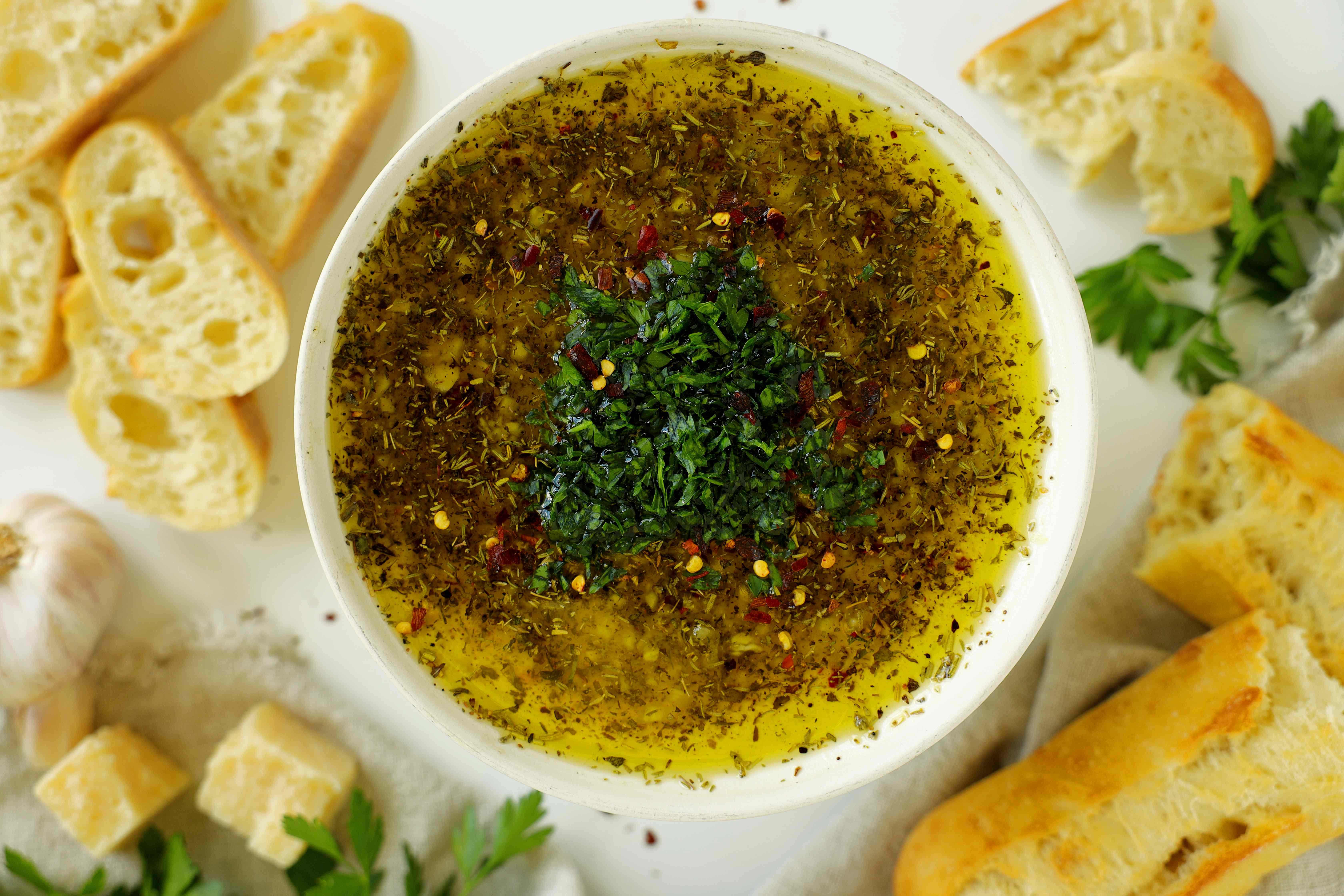 Overhead view of Italian-style bread dipping oil with herbs and red pepper flakes, served with sliced bread.
