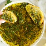 Overhead view of homemade bread dipping oil with two slices of seasoned bread and fresh parsley.