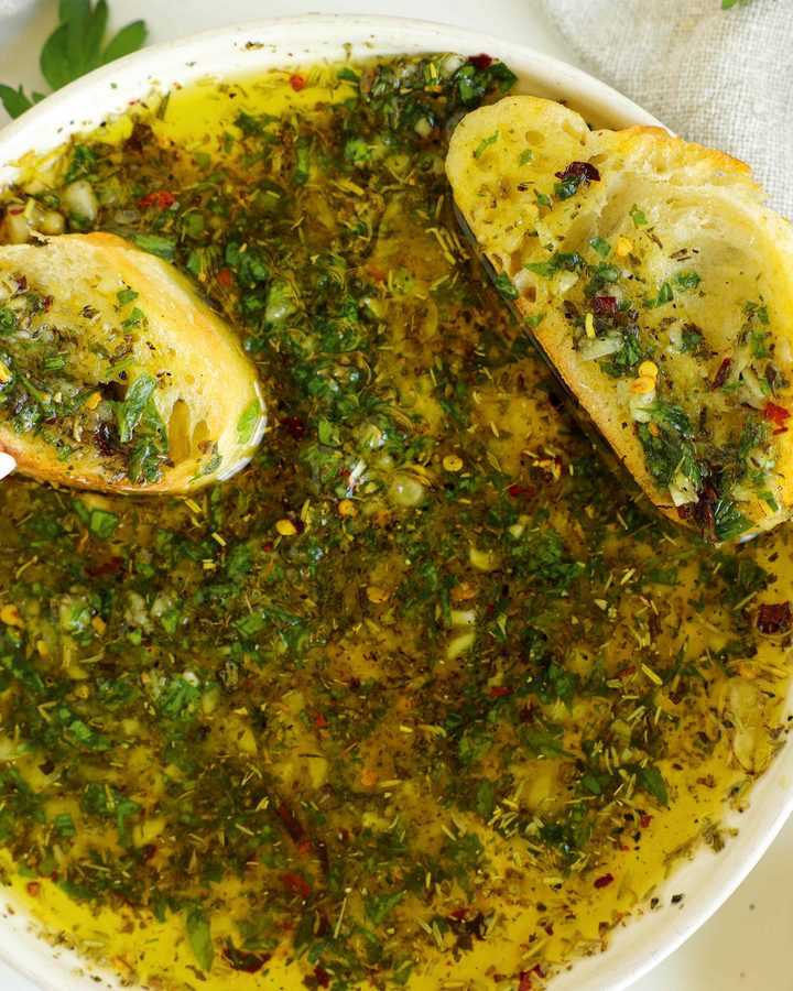 Overhead view of homemade bread dipping oil with two slices of seasoned bread and fresh parsley.