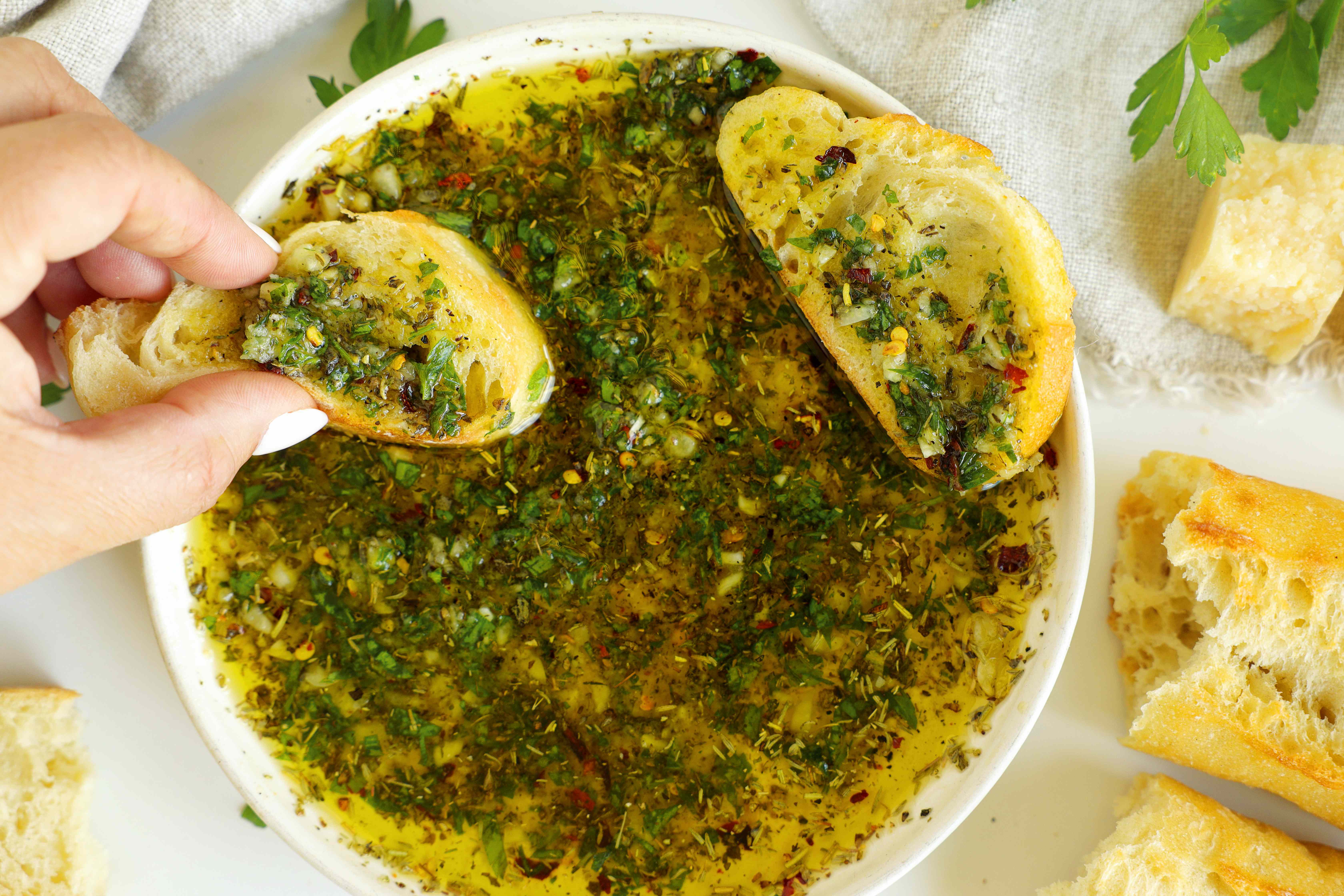 Overhead shot with two pieces of bread coated in the dipping oil, one being held over the bowl.