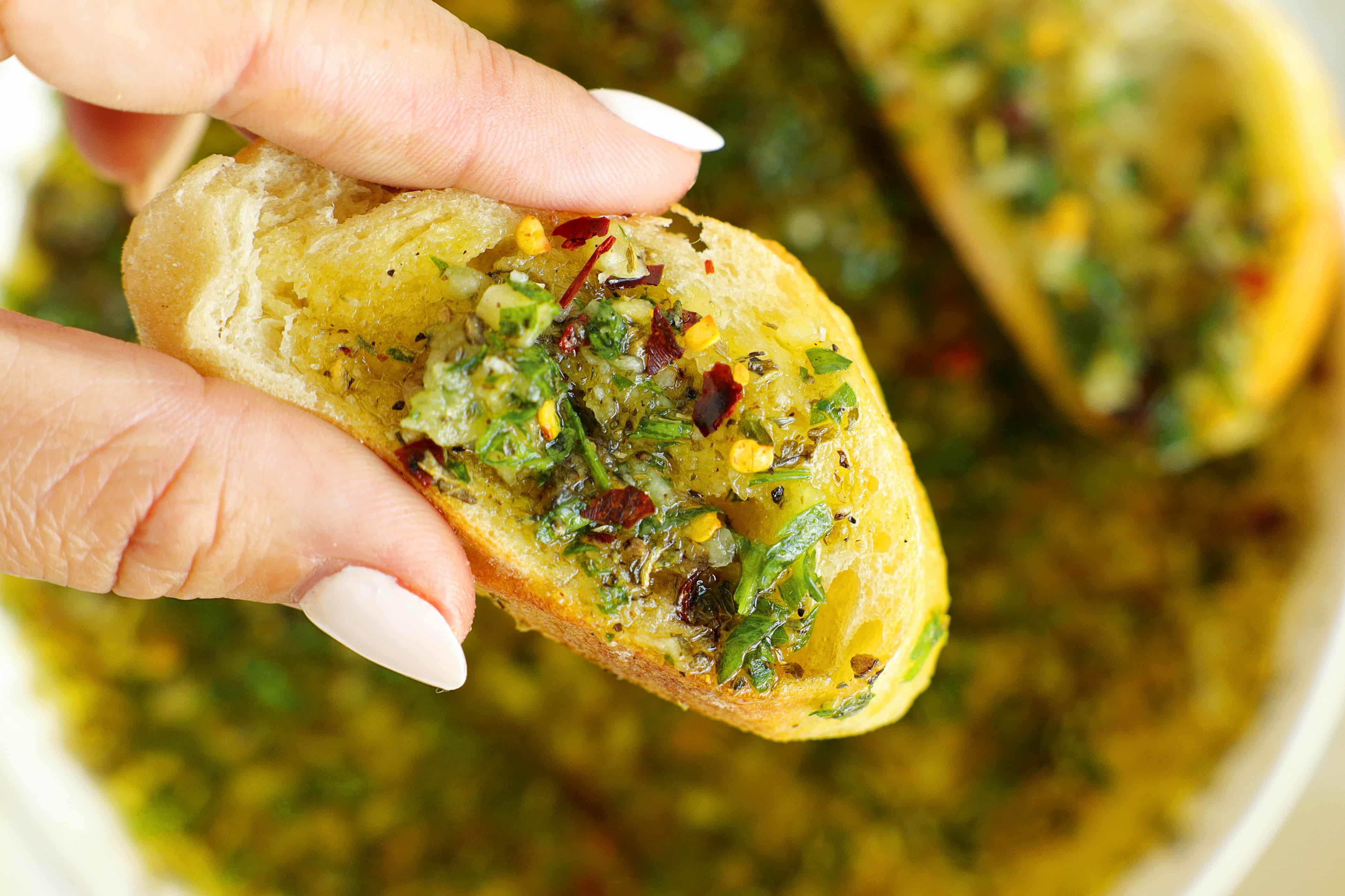 Homemade bread dipping oil in a white bowl surrounded by crusty baguette slices and fresh parsley.