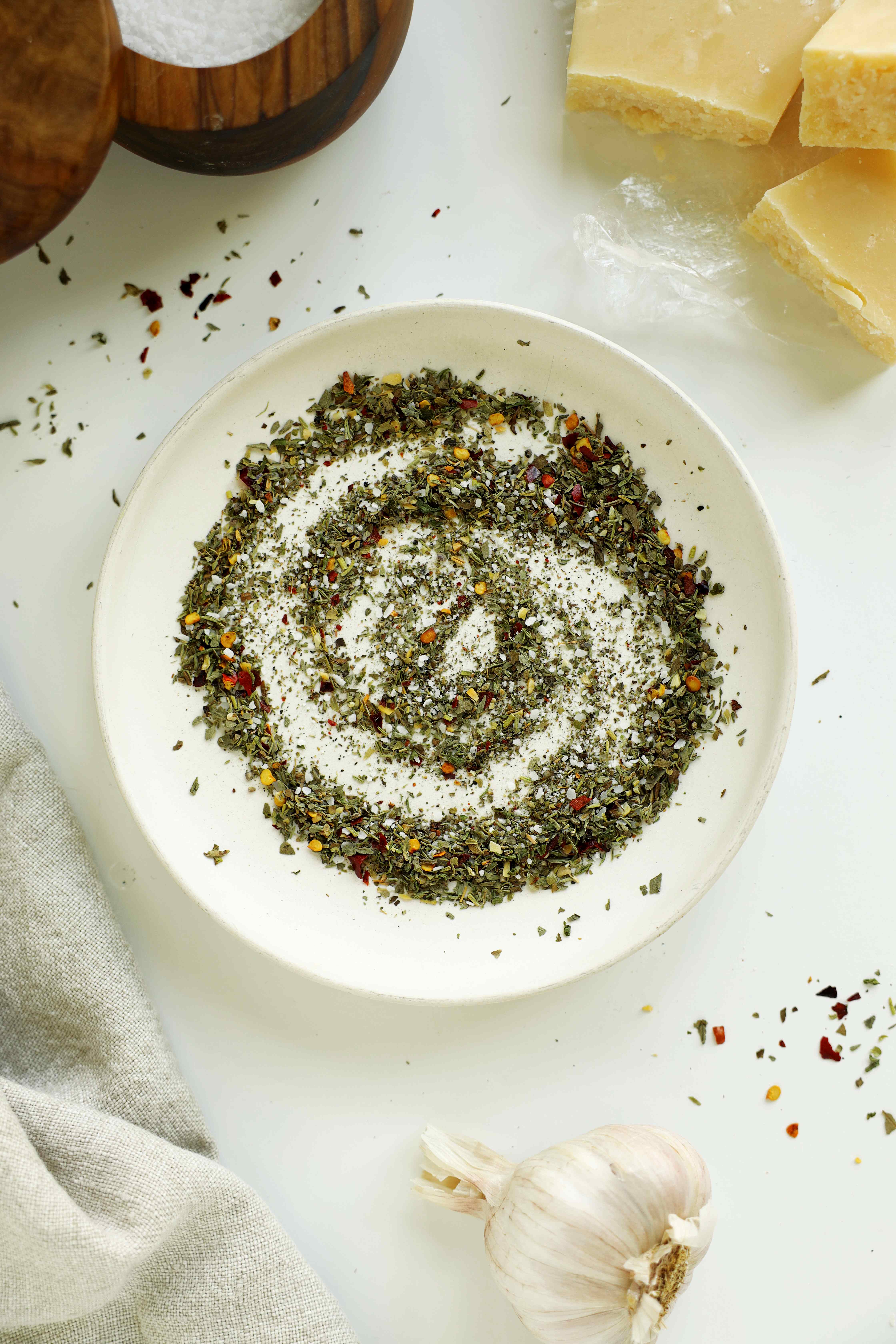 Italian herbs, crushed red pepper flakes, and seasonings in a white bowl before adding olive oil.