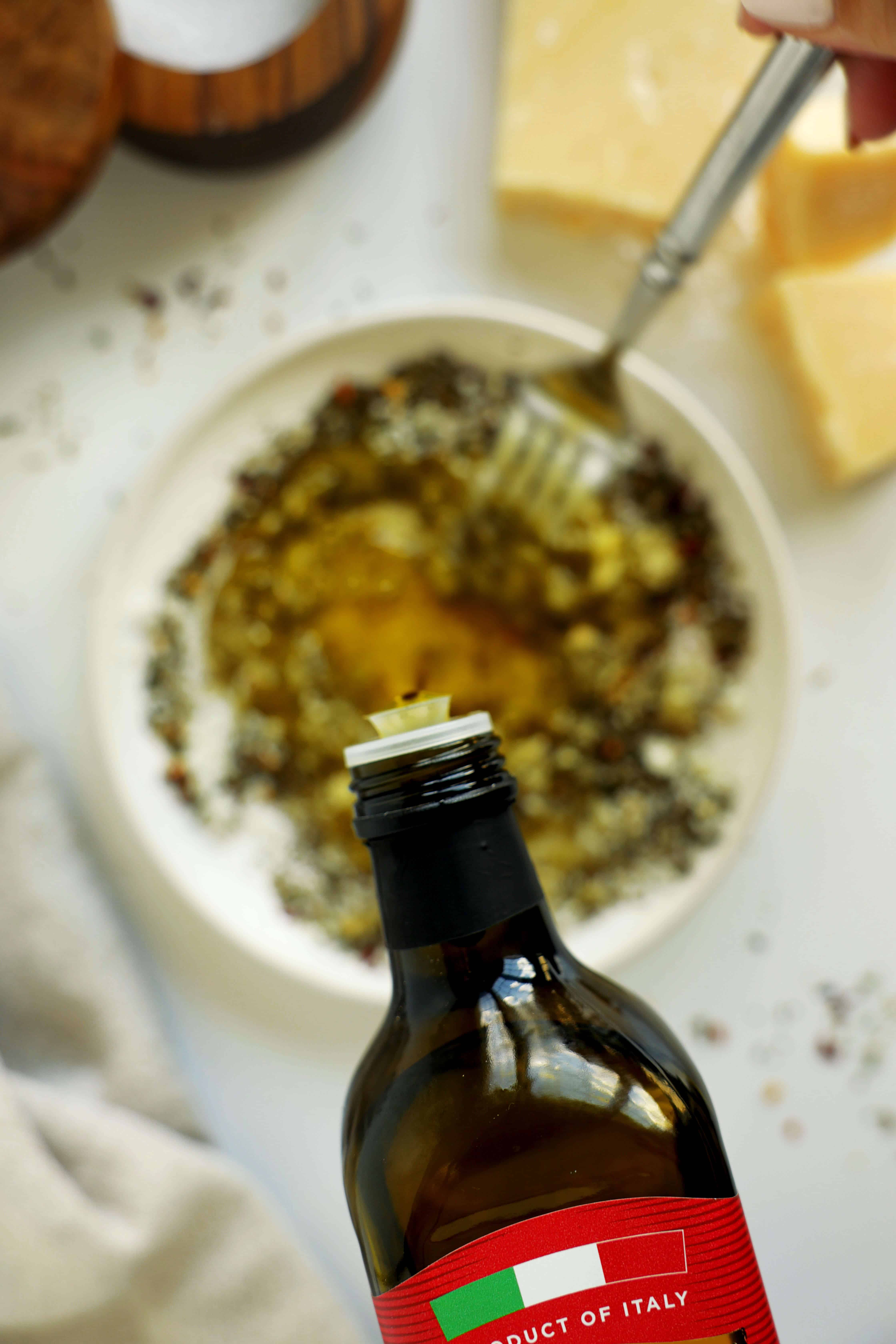 Olive oil poured into a bowl of herbs, garlic, and Parmesan cheese to make bread dipping oil.