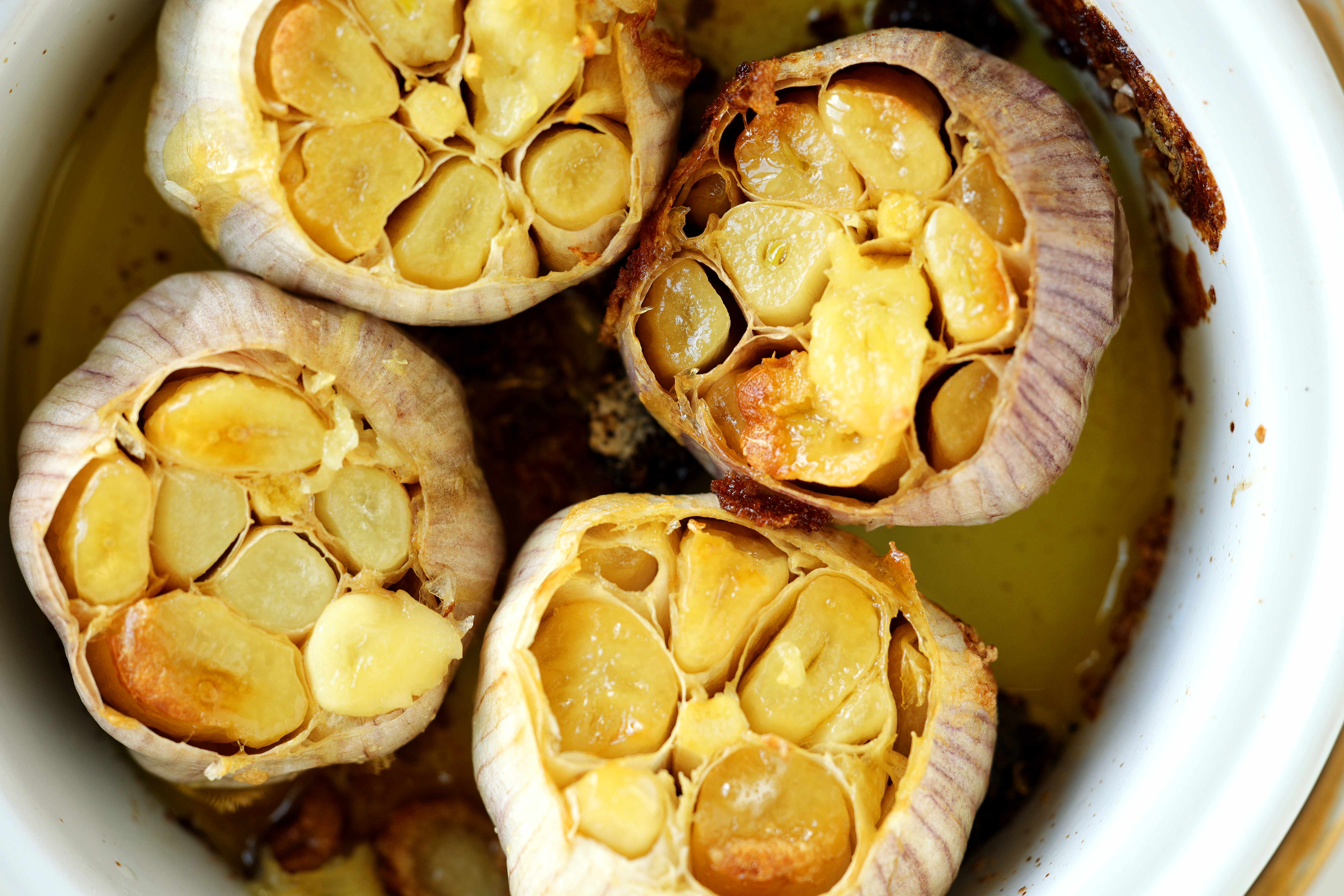 Close-up overhead view of four roasted garlic bulbs with soft, golden cloves in olive oil.