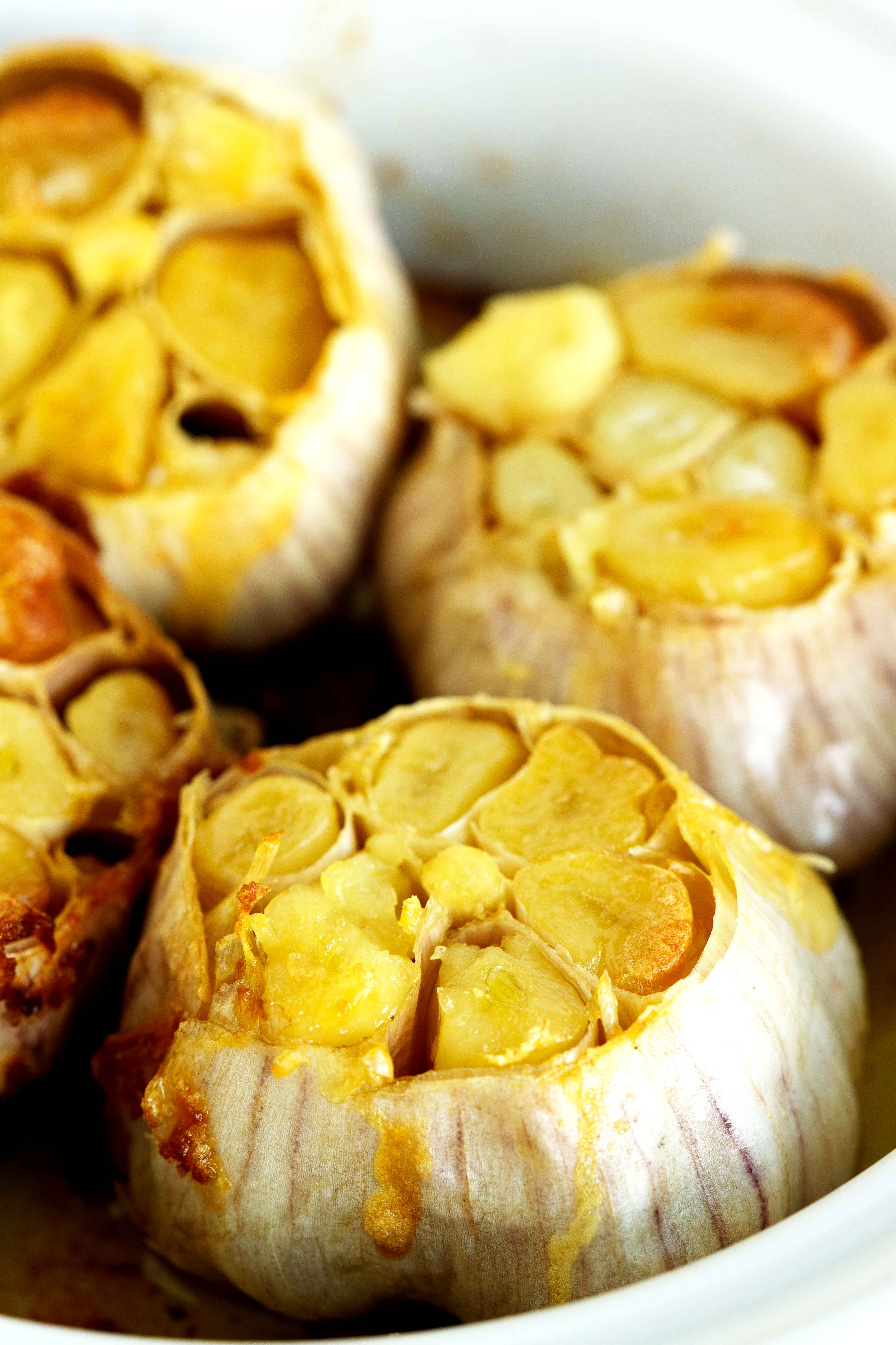 Close-up of whole roasted garlic bulbs with tender, golden cloves in a baking dish.