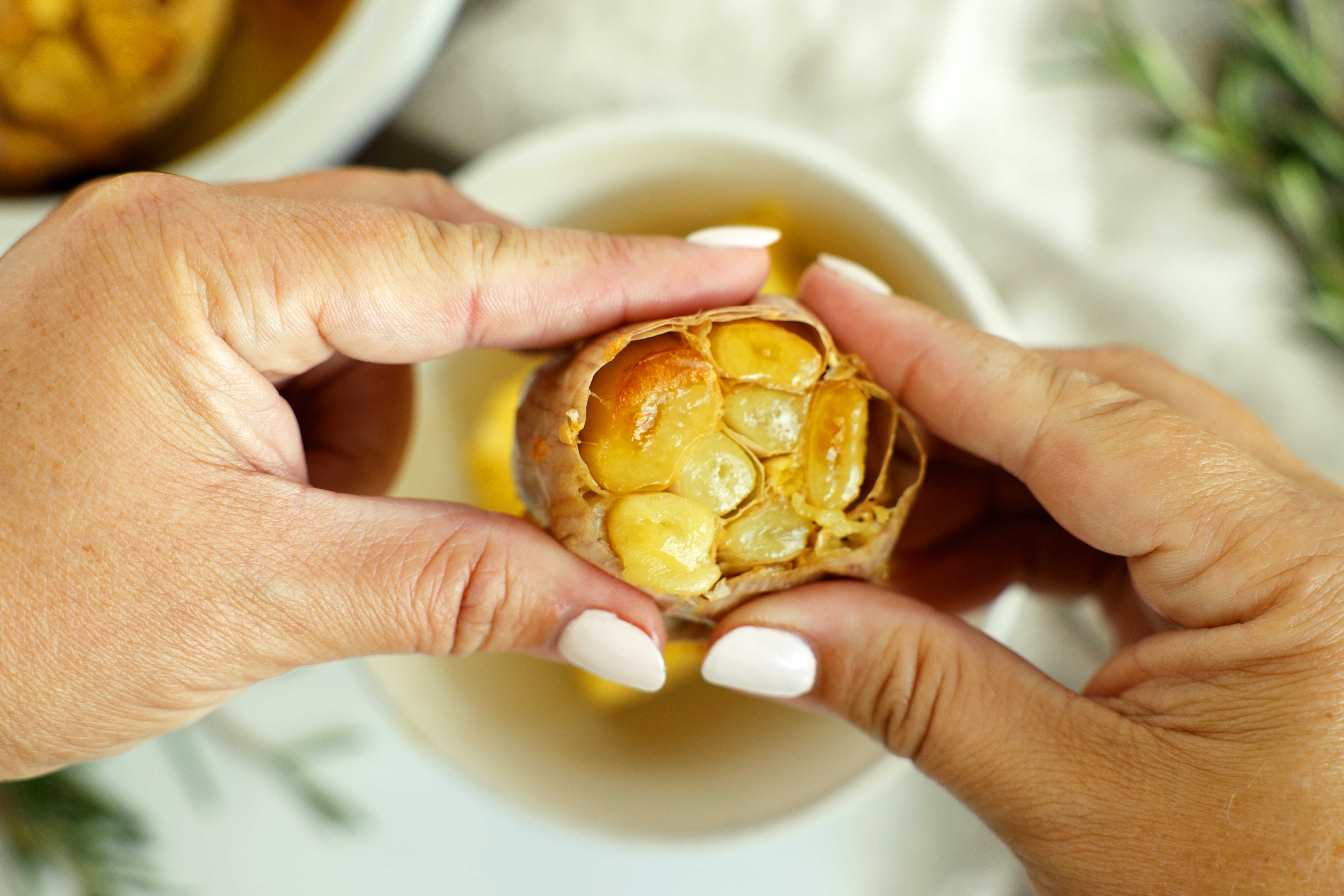 Hands holding a roasted garlic bulb with golden, caramelized cloves exposed.