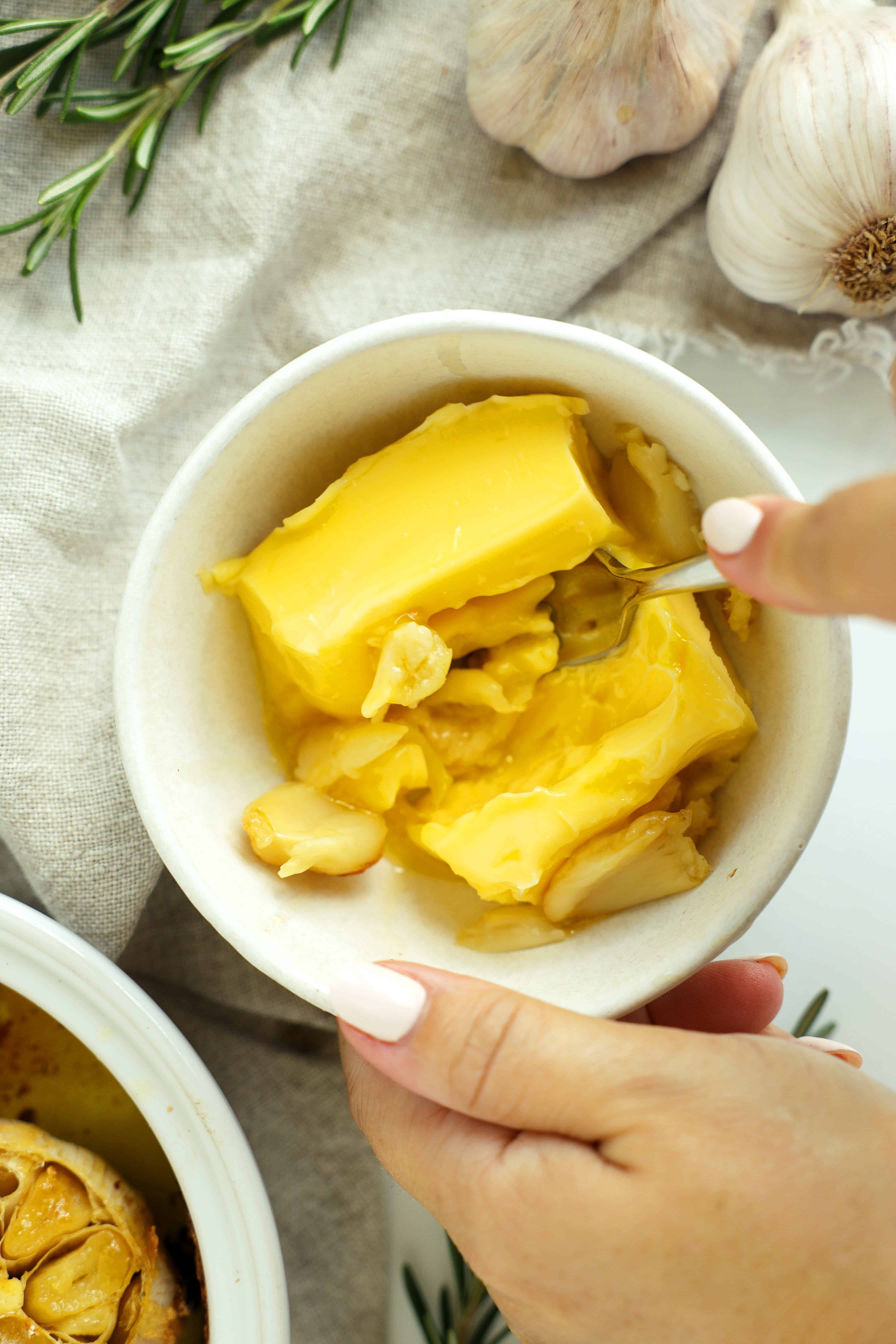 Softened butter and roasted garlic cloves being mashed together with a fork.